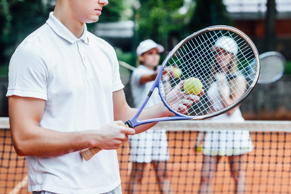 a man swinging a tennis racket with both hands, with two tennis girls in the background