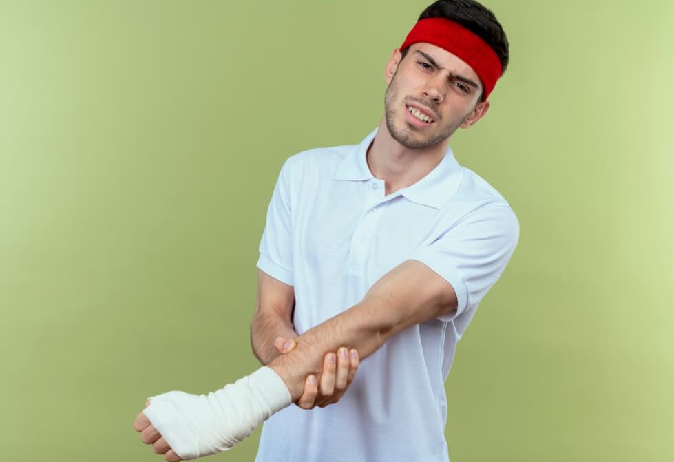 man in red headband holding his elbow with hand in front of green wall