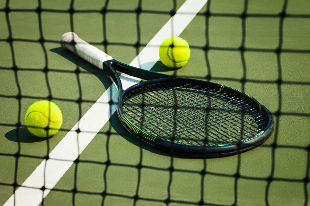 Shadowed racket and ball behind net on green court